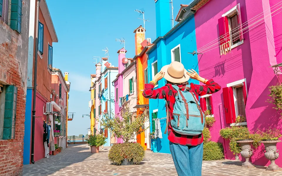 Visitor walking past bright pink and blue houses in Burano