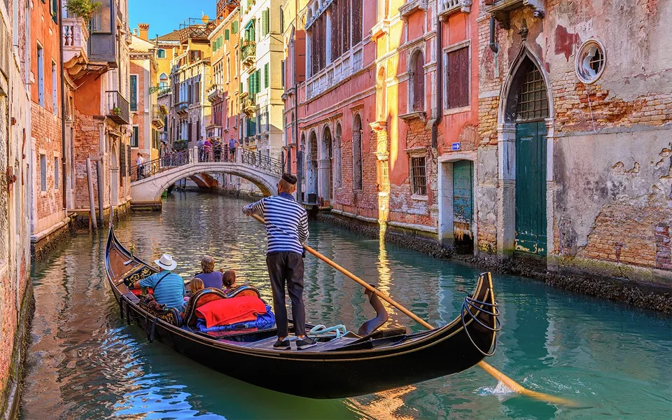Gondolier rowing along a narrow canal lined with colourful buildings